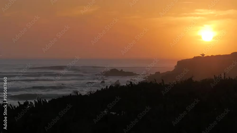 Two surfers walking towards the setting sun at the coastline of Morocco