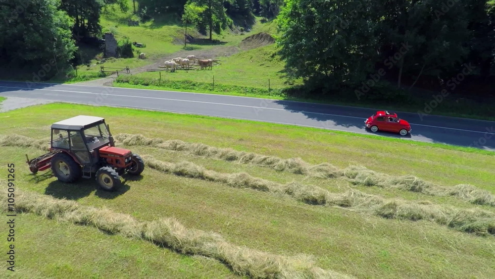 Red retro zastava passes a tractor when it is hay harvesting Red retro zastava passes a tractor when it is hay harvesting