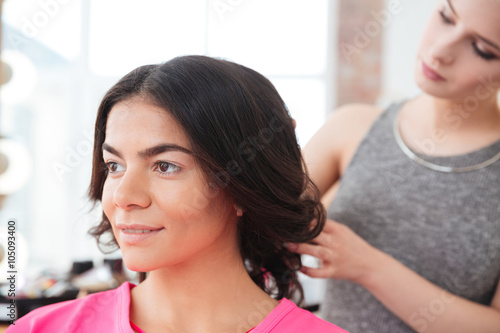 Woman hair stylist making hairstyle to young female model