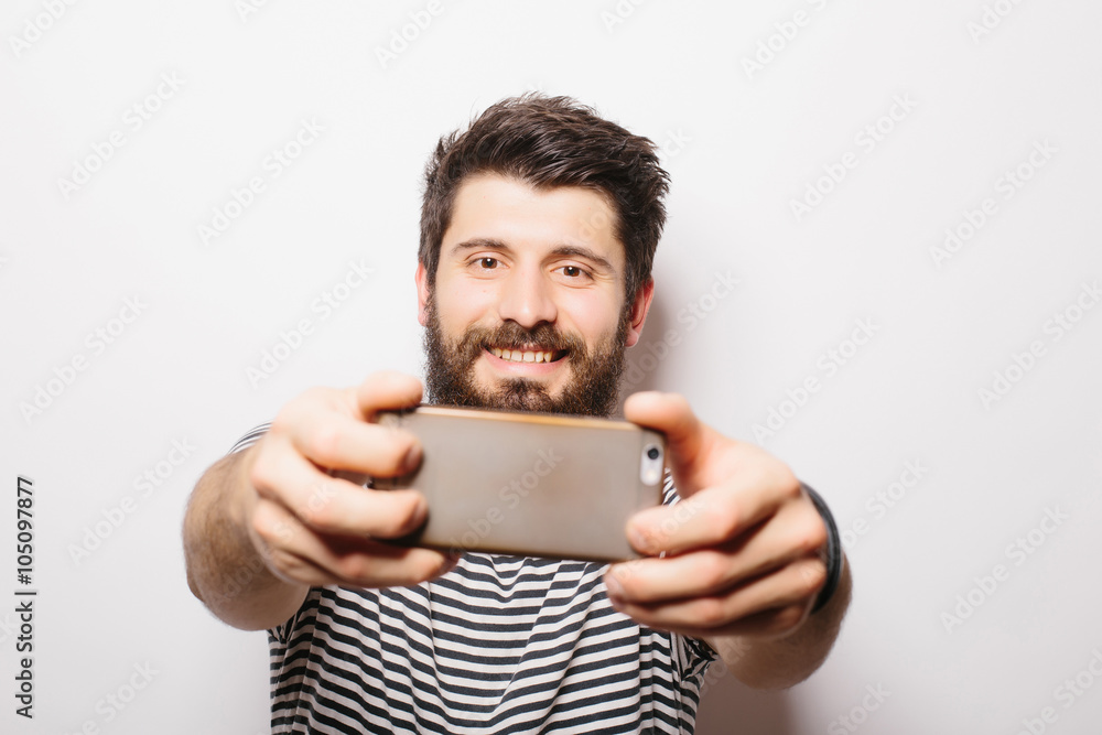 Hipster man with beard standing on white isolated background and taking face selfie with mobile phone . Hipster man with beard standing on white isolated background and taking face selfie with mobile phone .