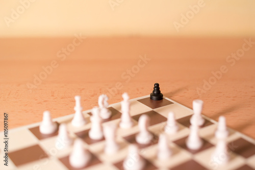 Chess pieces as metaphor - racism and bullying, one black piece is in the corner surrounded by big majority of white pieces photo