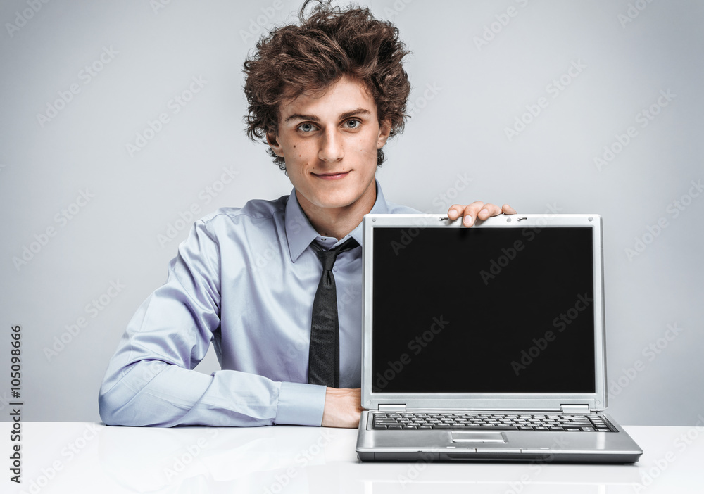 Friendly young manager is glad to see the client. Smiling businessman at the workplace looking at camera on gray background Friendly young manager is glad to see the client. Smiling businessman at the workplace looking at camera on gray background
