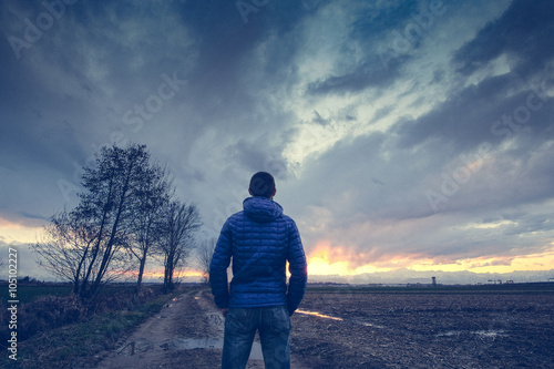     Man under a cloudy sky in the country watching the sunset  photo