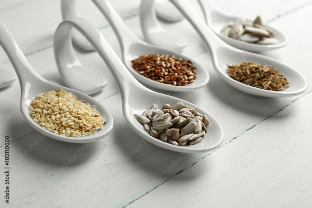 Different kinds of seeds in spoons on wooden table Different kinds of seeds in spoons on wooden table