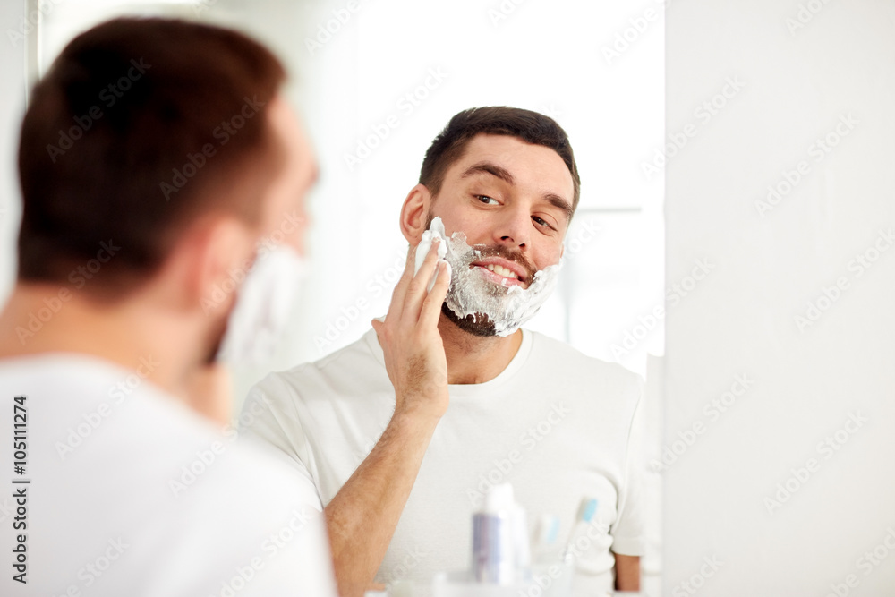 happy man applying shaving foam at bathroom mirror