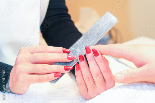 Manicure to man fingernails by professional manicurist woman in beauty salon - Closeup of young woman hands with red nail polish using file - Concept of male beauty care 