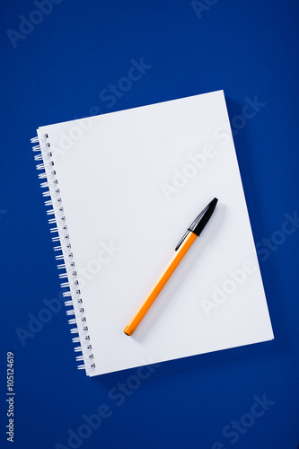 White spiral notepad with ball pen on blue background