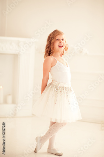 Laughing kid girl 4-5 year old standing in white room. Wearing gymnastic leotard and fluffy skirt. Looking at camera. Childhood. 