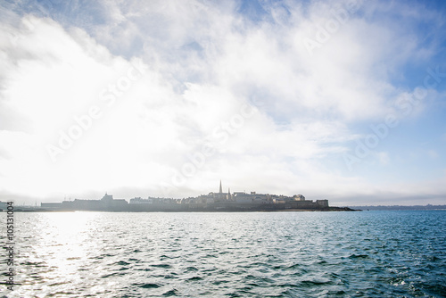 view of the fortified city of Saint-Malo behind behind the sea during a sunny day seen from a boat off the coast of brittany