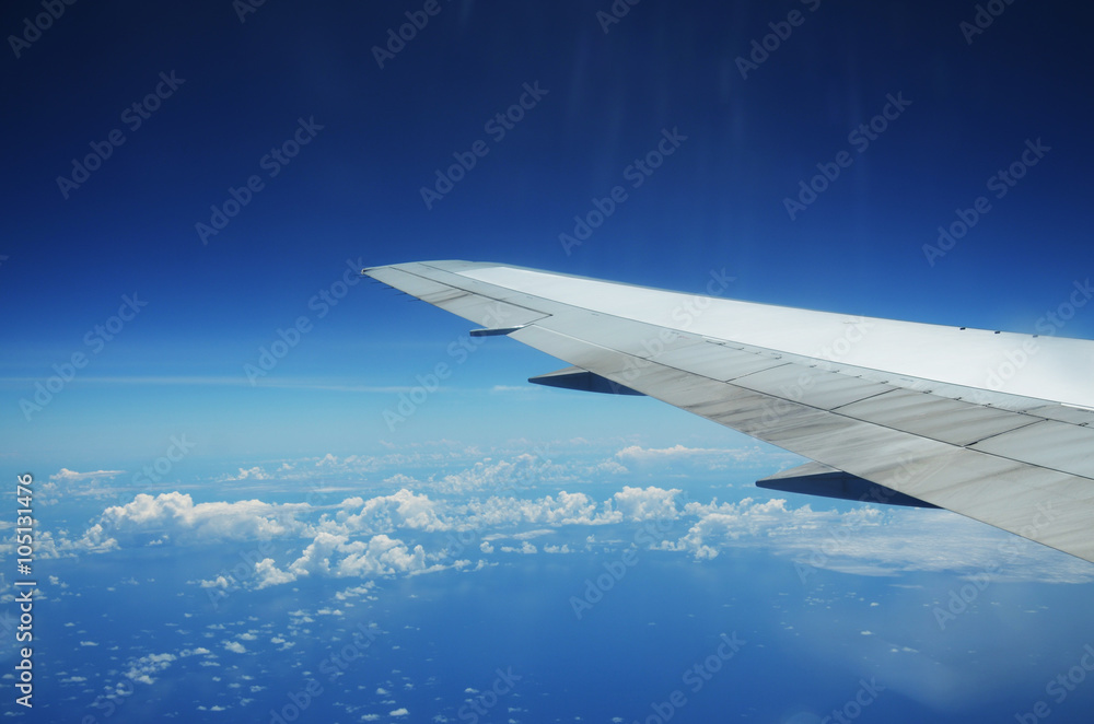 Obraz premium Wing of an airplane flying above the clouds over tropical island