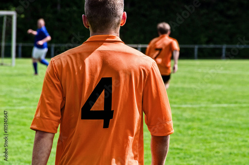 Fußballspieler auf dem Spielfeld im orangenTrikot von hinten