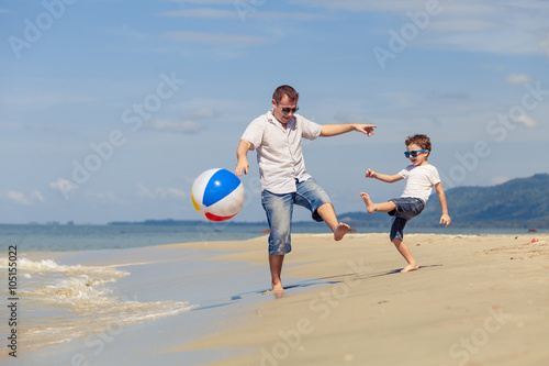 Father and son with ball playing soccer on the beach at the day