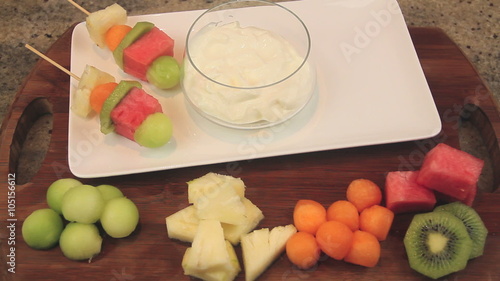 Serving fruit kebabs on a plate with with a yogurt dipping sauce.
