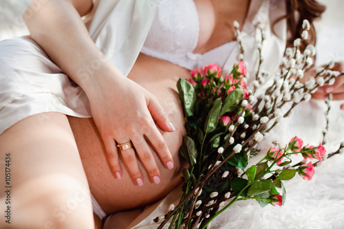 pregnant woman in white lingerie lying on the bed with flowers
