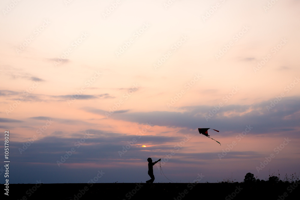 silhouette boy running and flying a kite