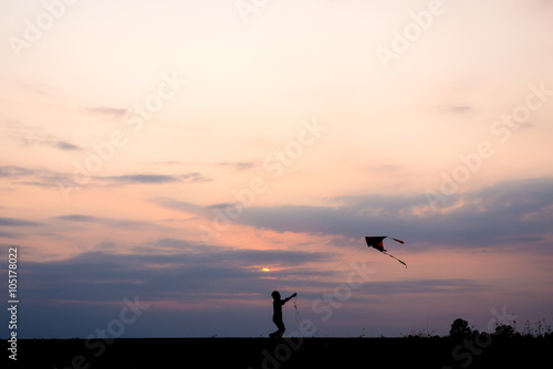 silhouette boy running and flying a kite