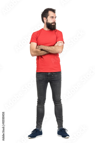 Young bearded guy in red t-shirt with crossed arms looking away. Full body length portrait isolated over white studio background.