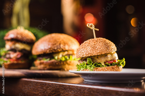 Three juicy tasty burger on the white plate on a dark background