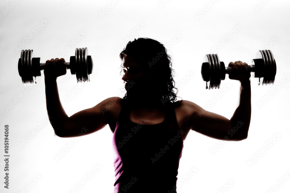 Partial silhouette of a female trainer holding dumbbells. Almost in a shoulder press.
Partial silhouette of a female trainer holding dumbbells. Almost in a shoulder press.