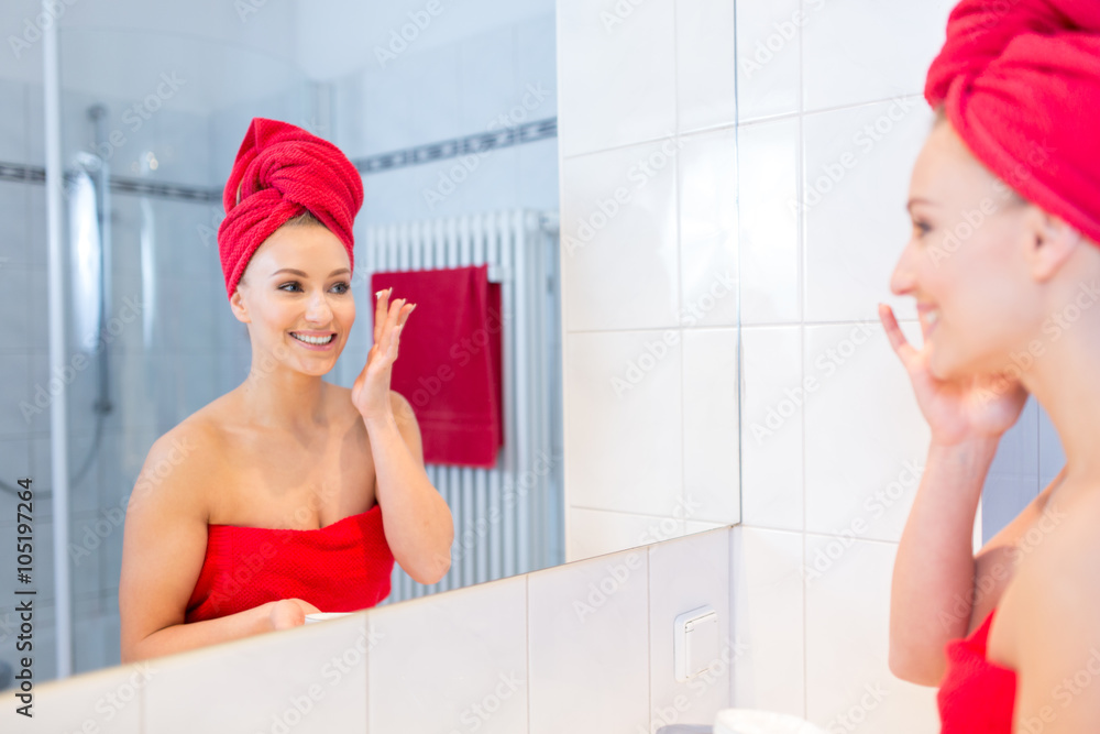 Junge Frau sieht im Badezimmer in den Spiegel, lächelt und pflegt sich und  ist nur mit Handtüchern bekleidet Stock Photo