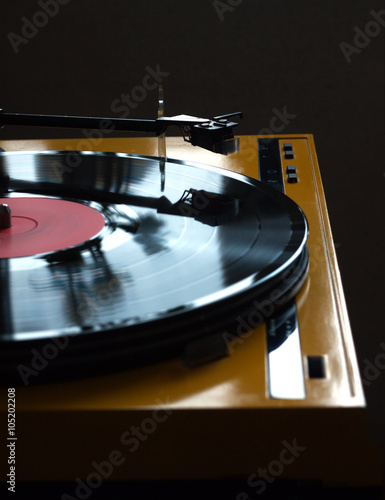 Funny turntable in yellow case with rotation vinyl record with red label isolated on dark background. Vertical photo side view closeup