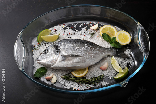 Dorado fish is in glass dish with salt, rosemary, garlic, lime a