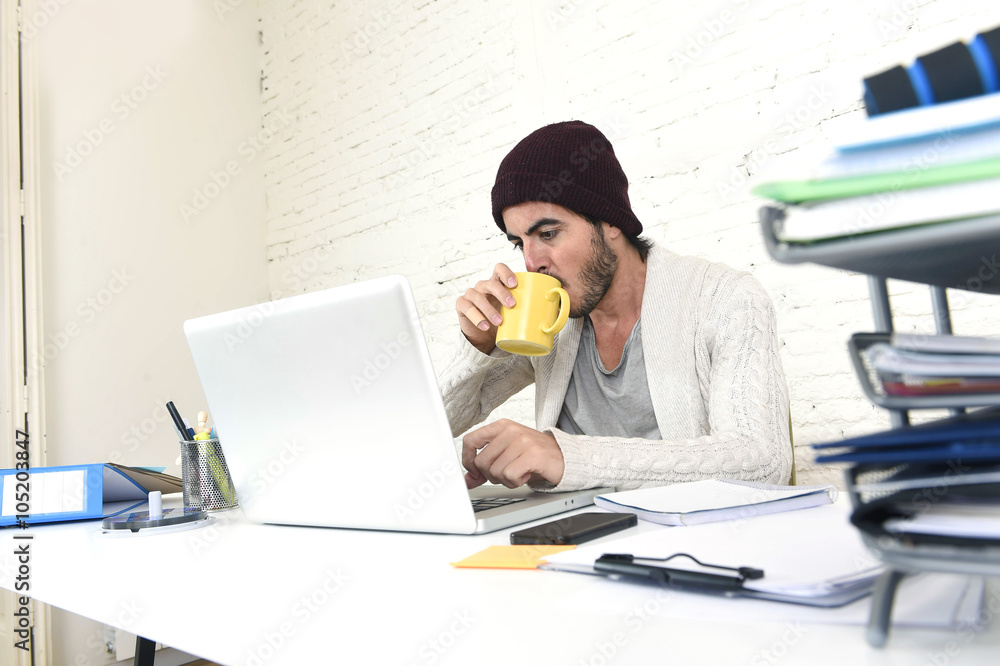 trendy businessman in cool hipster beanie drinking coffee working in at modern home office with computer trendy businessman in cool hipster beanie drinking coffee working in at modern home office with computer