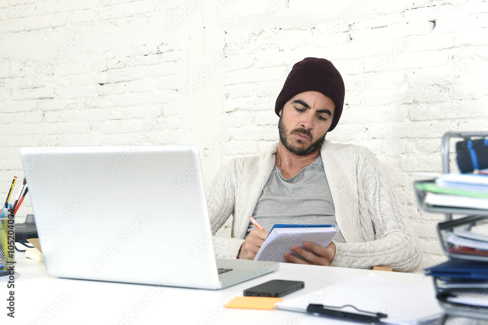 trendy businessman in cool hipster beanie writing on pad working in at modern home office with computer trendy businessman in cool hipster beanie writing on pad working in at modern home office with computer