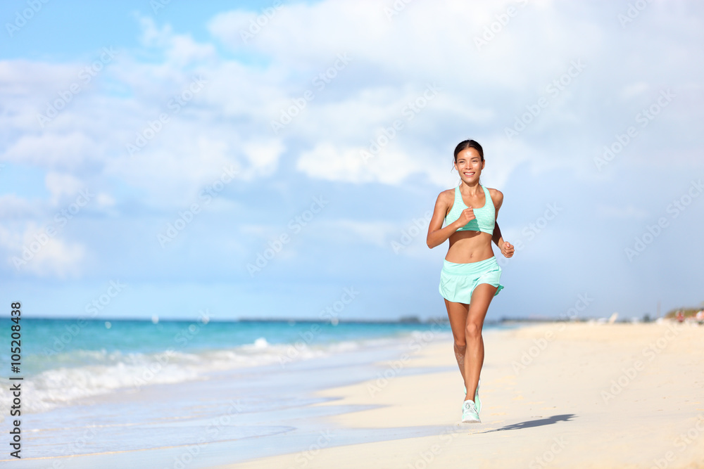 Happy fit female runner running on sand during summer travel vacation on tropical beach. Asian woman jogging doing cardio training exercising for weight loss. Happiness and wellbeing concepts. Happy fit female runner running on sand during summer travel vacation on tropical beach. Asian woman jogging doing cardio training exercising for weight loss. Happiness and wellbeing concepts.