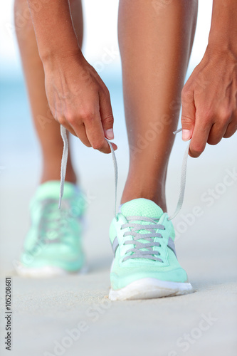 Sportswoman runner getting ready tying running shoes on beach. Fitness woman living a healthy and active life preparing for cardio training. Wellness and health concept.