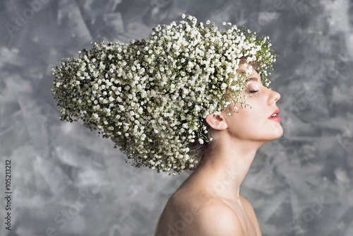 Portrait of young woman with hairstyle made of white baby flowers on gray background