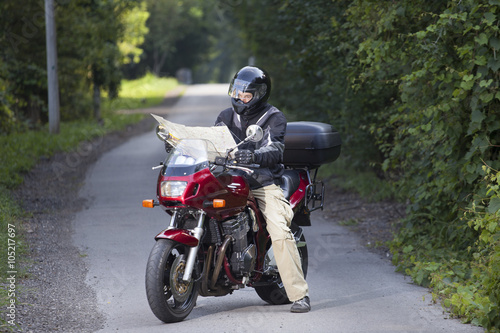 Motorcyclist lost on the road through the forest looking at map