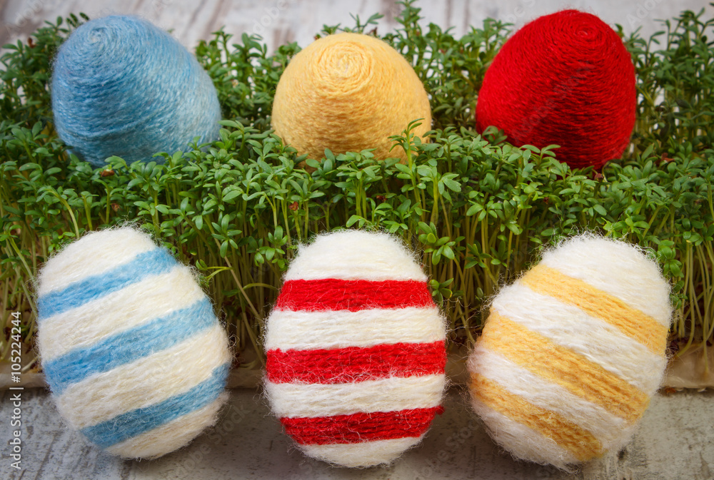 Fototapeta premium Easter eggs wrapped woolen string and green cress on wooden background, decoration for Easter
