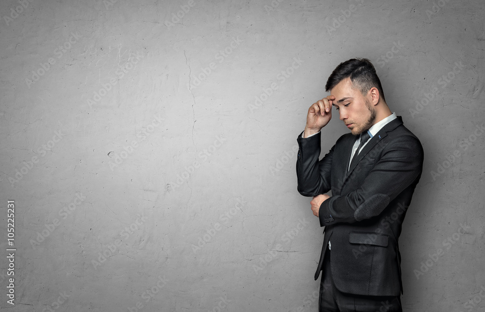 Young man in business suit, thinking about something, on concrete wall background. Business concept Young man in business suit, thinking about something, on concrete wall background. Business concept