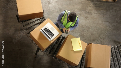 Man in shipping warehouse uses laptop, overhead view