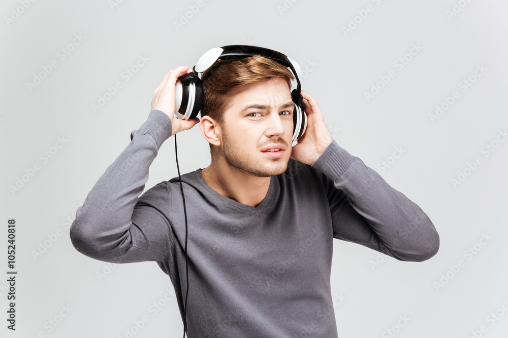 Handsome young man in grey pullover taking off headphones Stock