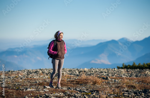 Portrait of young tourist walking on rocky mountains enjoying nature on backpacking trip. Beautiful mountains on background. Girl looking into distance. Sunny fall day