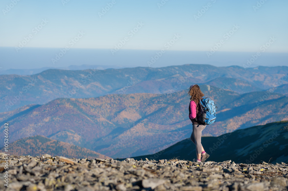 Young athletic woman backpacker standing on the ridge of the mountain enjoying the open view on the big mountains. Rear view, sunny autumn day.