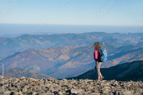 Young athletic woman backpacker standing on the ridge of the mountain enjoying the open view on the big mountains. Rear view, sunny autumn day.