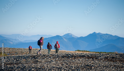 Group/team of four young athletic tourists walking on the rocky mountain plato on their backpacking trip. Woman is talking on the phone. Beautiful mountains on background. Healthy lifestyle