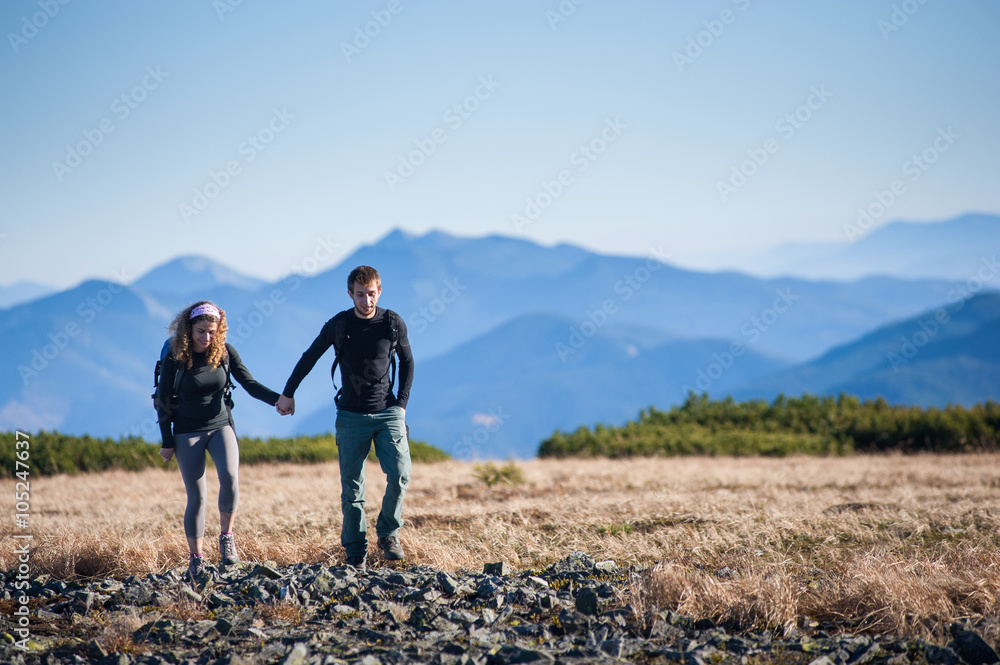 Young couple of tourists hiking in the beautiful mountains on warm sunny fall day. Man and woman holding hands.