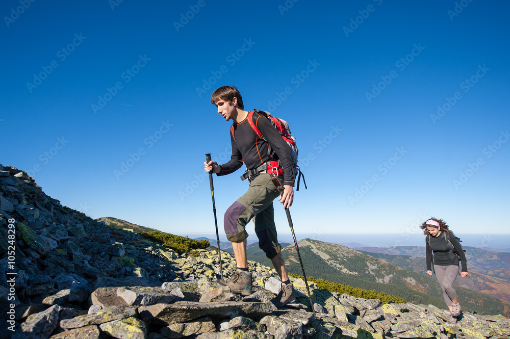 Young hiker couple climbing up rocky the mountain top, high altitude. Beautiful autumn mountain landscape on the background. Fall.
