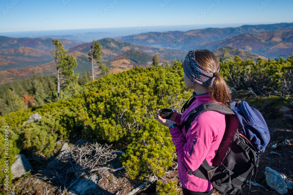 Young female backpacker resting on mountain peak with cup of tea/coffee, enjoying view of valley below. Colorful autumn time. Young female backpacker resting on mountain peak with cup of tea/coffee, enjoying view of valley below. Colorful autumn time.