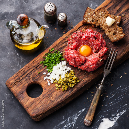 Schilderij op canvas Beef tartare steak with pickled cucumber and onion on dark marbl