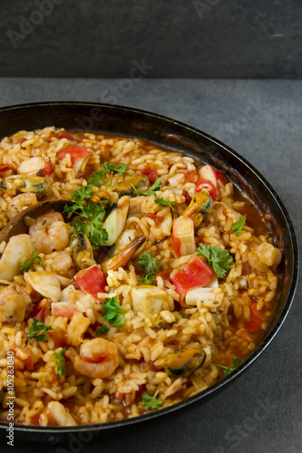 Spanish dish called paella with seafood, on the pan, grey background.