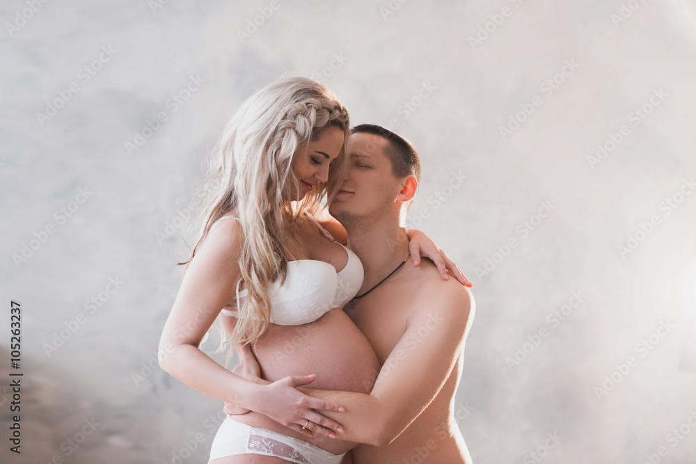Husband hugging his pregnant wife in white lingerie on a light background,  lifestyle, waiting, belly Stock Photo