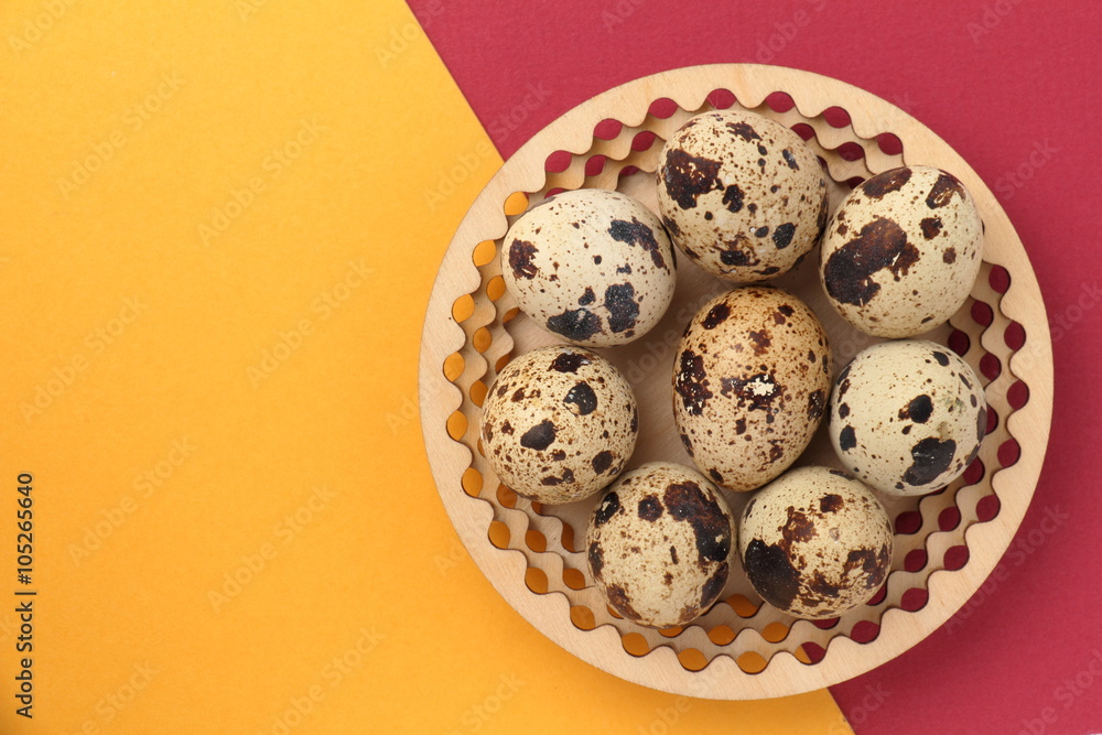 Easter background. / Quail eggs on a wooden plate. Yellow and red background.