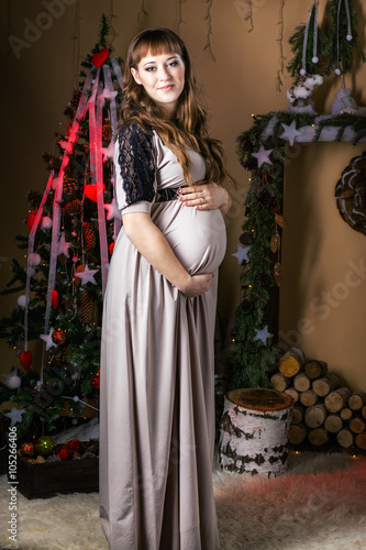 Young beautiful pregnant woman in a long dress near new year tr