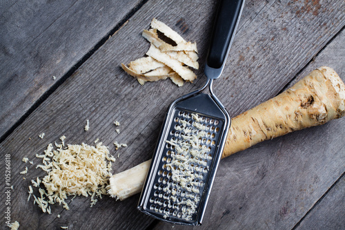 Valokuva Grated horseradish root with grater on wooden gray table.