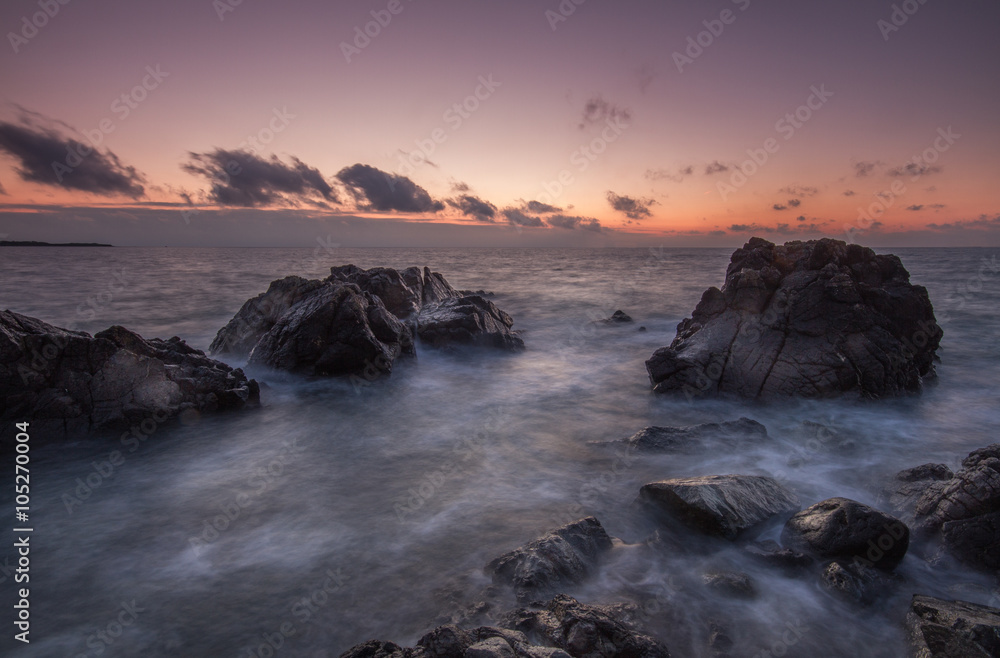An early morning sunset over rugged rocks in Corneall. A long exposure image of a rocky coastline seascape with waves flowing over hard, dark rocks. An early morning sunset over rugged rocks in Corneall. A long exposure image of a rocky coastline seascape with waves flowing over hard, dark rocks.